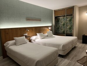 Une chambre d’hôtel avec deux lits, une tête de lit en bois, un mur orné d’un motif texturé vert et une grande armoire décorée d’une fresque aux motifs tropicaux.