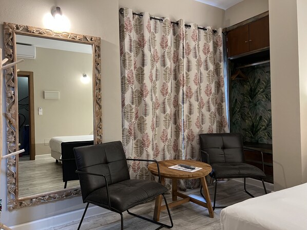 Une pièce comprenant deux fauteuils en cuir, une table en bois, un grand miroir et un rideau orné d’un motif de feuilles.