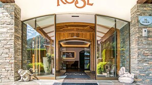 La entrada del Hotel Rose, con fachada de piedra, puertas de cristal y un arco de madera.