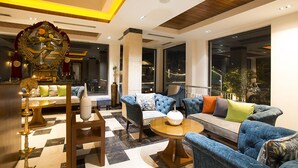 Eine moderne Lobby mit Schachbrettmuster-Boden, einer zentralen Sitzecke mit blau gepolsterten Sofas, einer dekorativen goldenen Statue und einem großen Fenster mit Blick ins Freie.