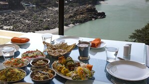 Ein Tisch, gedeckt für eine Mahlzeit, mit verschiedenen Speisen und Blick auf einen Fluss und ein Waldgebiet.