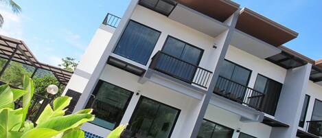 A modern multi-story building with balconies, large windows, and a swimming pool.