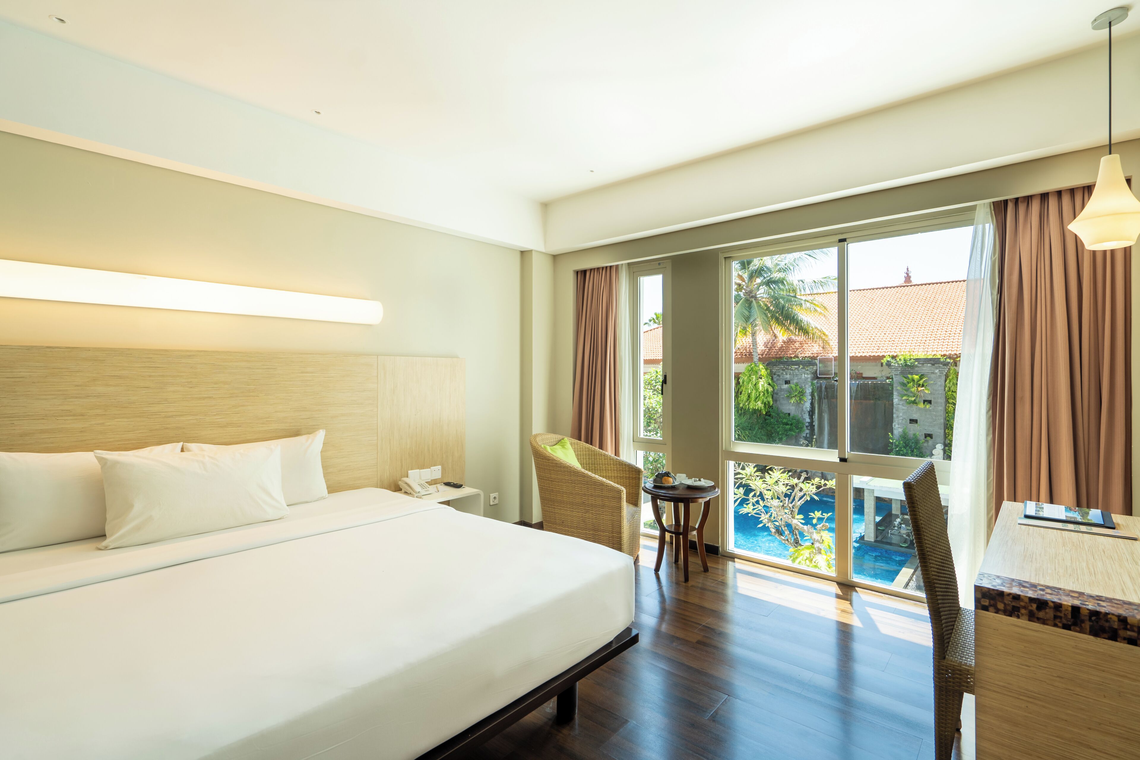 Quarto de hotel com uma cama grande, área de refeições com mesa e cadeiras, e vista para uma piscina.