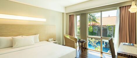 Quarto de hotel com uma cama grande, área de refeições com mesa e cadeiras, e vista para uma piscina.
