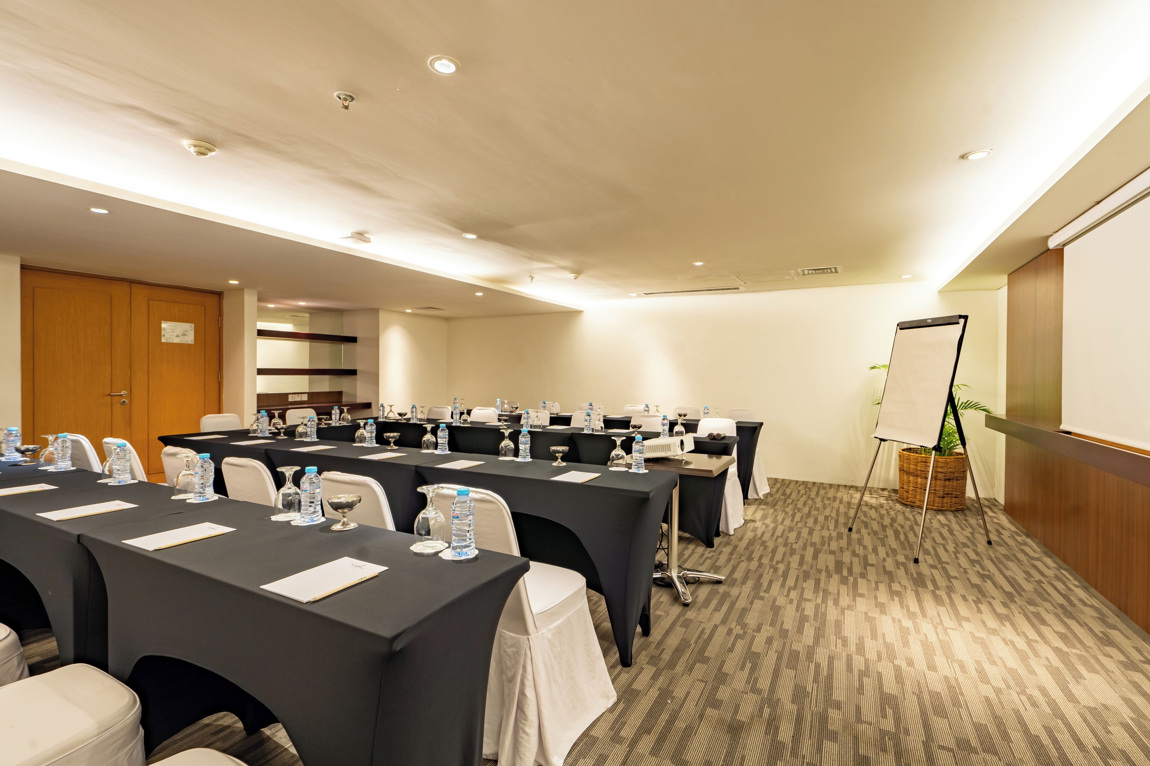 Un salón de conferencias con mesas, sillas, botellas de agua y un caballete.