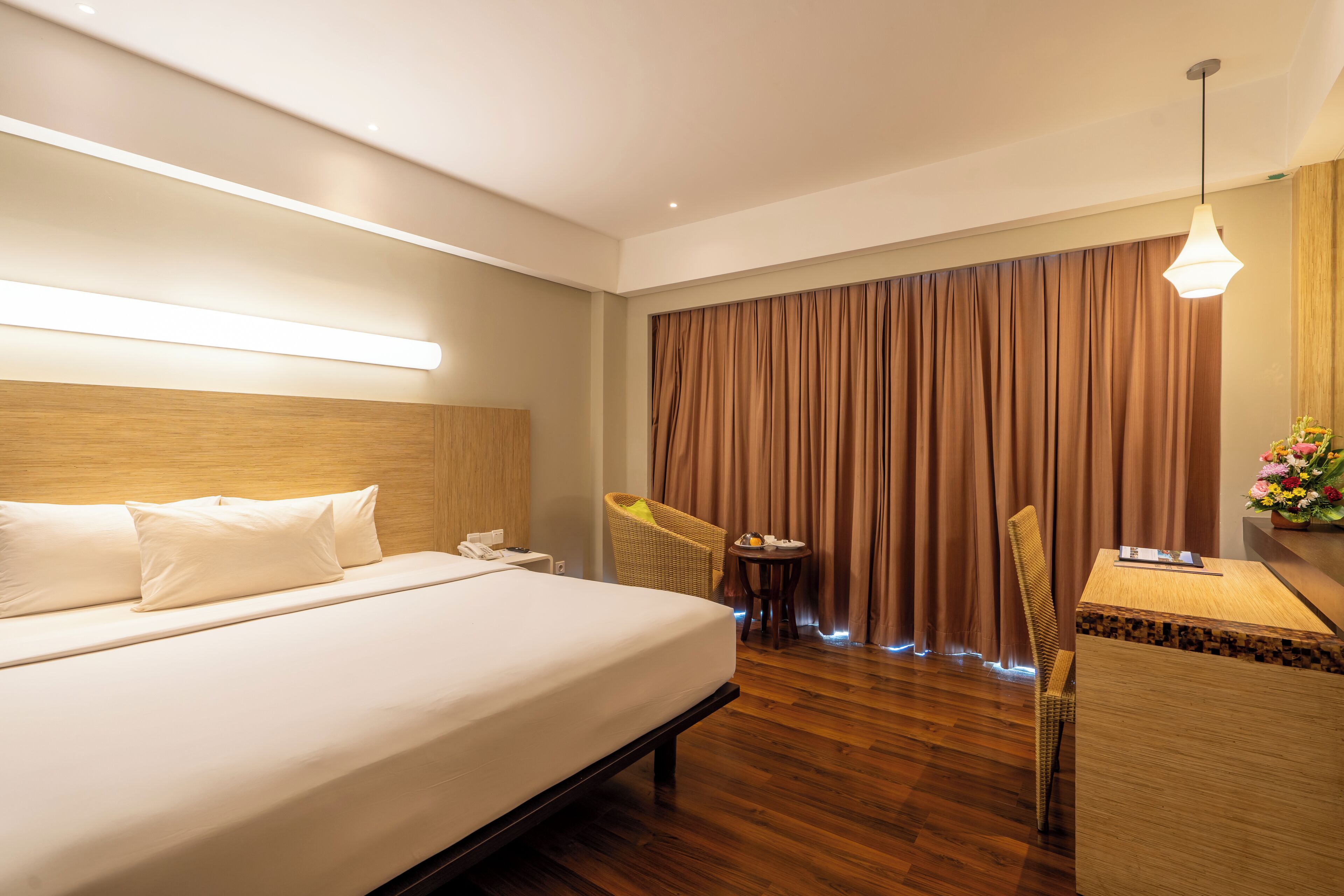 Habitación de hotel con una cama grande, un escritorio con silla, una mesita con otra silla y un amplio ventanal con cortinas.
