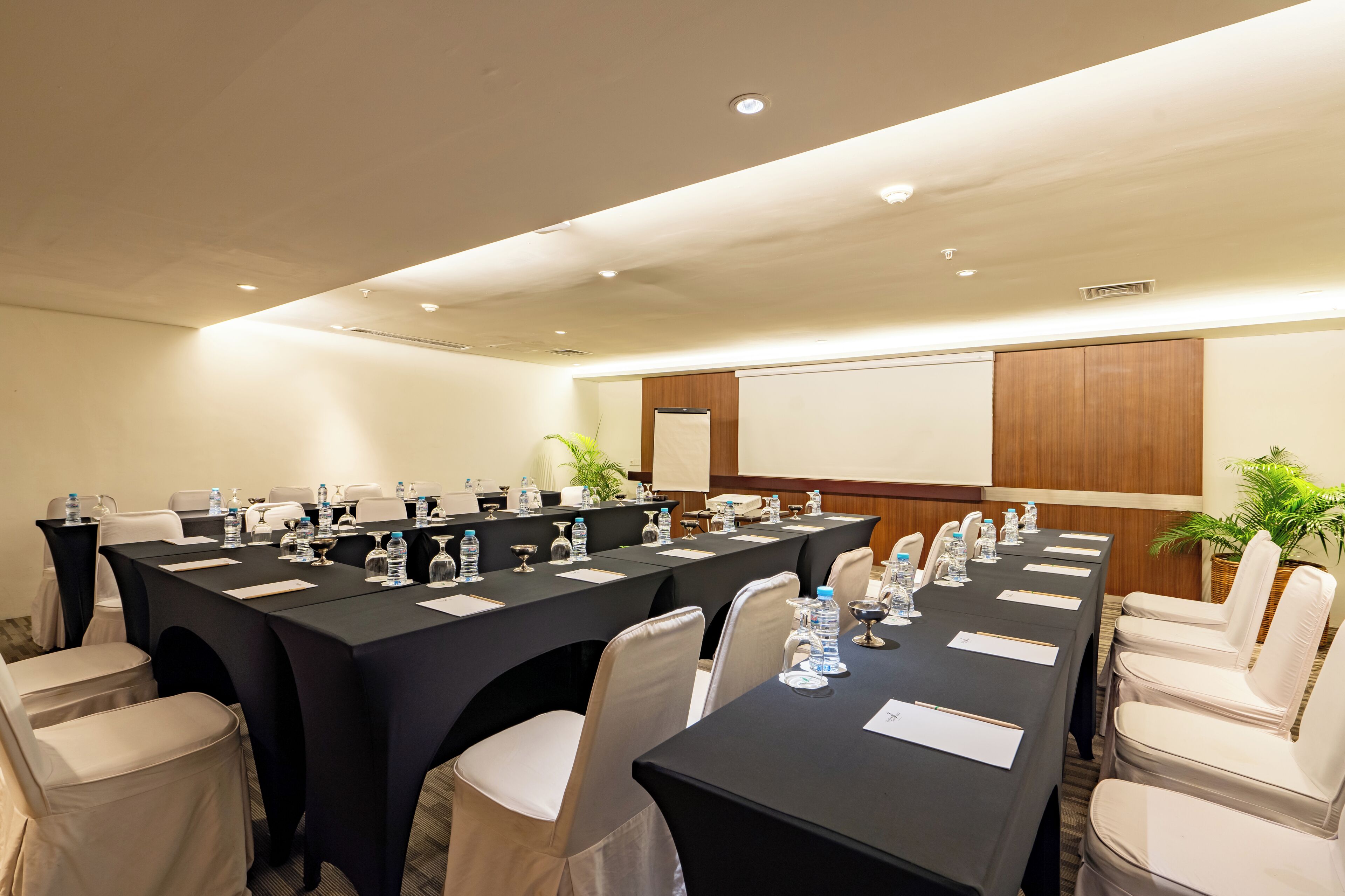 A conference room with multiple tables, chairs, water bottles, and a projector screen.