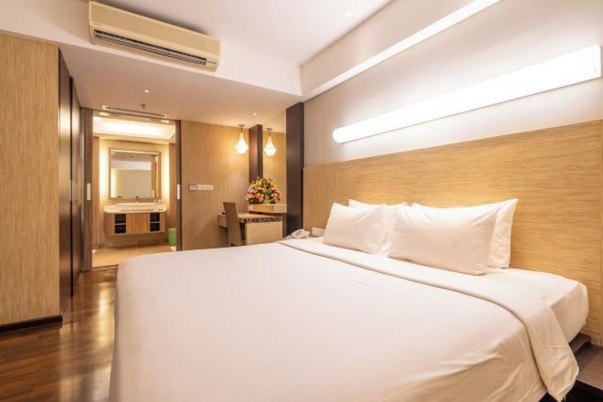 Una habitación de hotel con una cama grande, un cabecero de madera, una mesita de noche, un espejo y un pequeño escritorio con una silla.