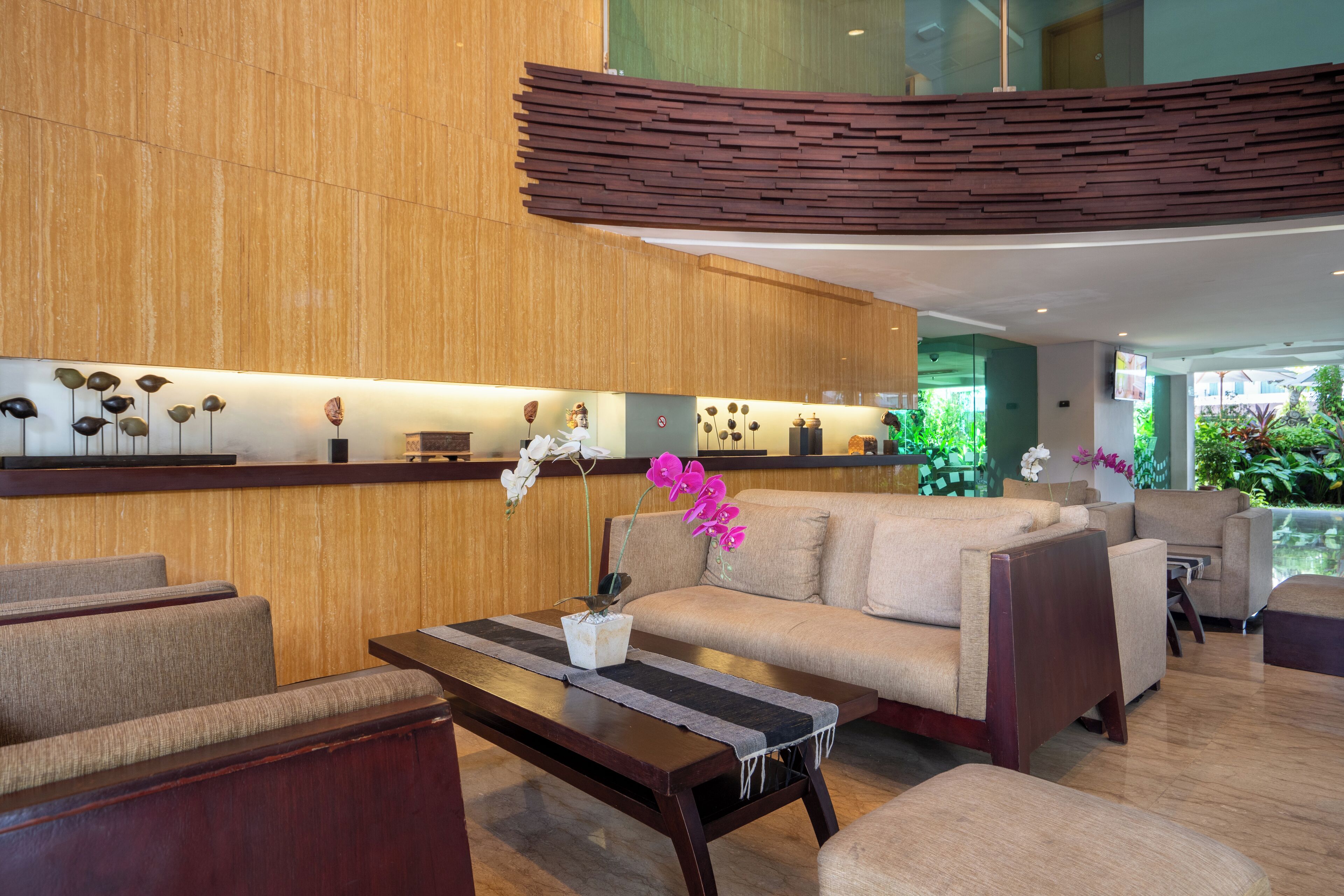 A modern lobby with a wooden reception desk, sofas, and a coffee table with orchids.