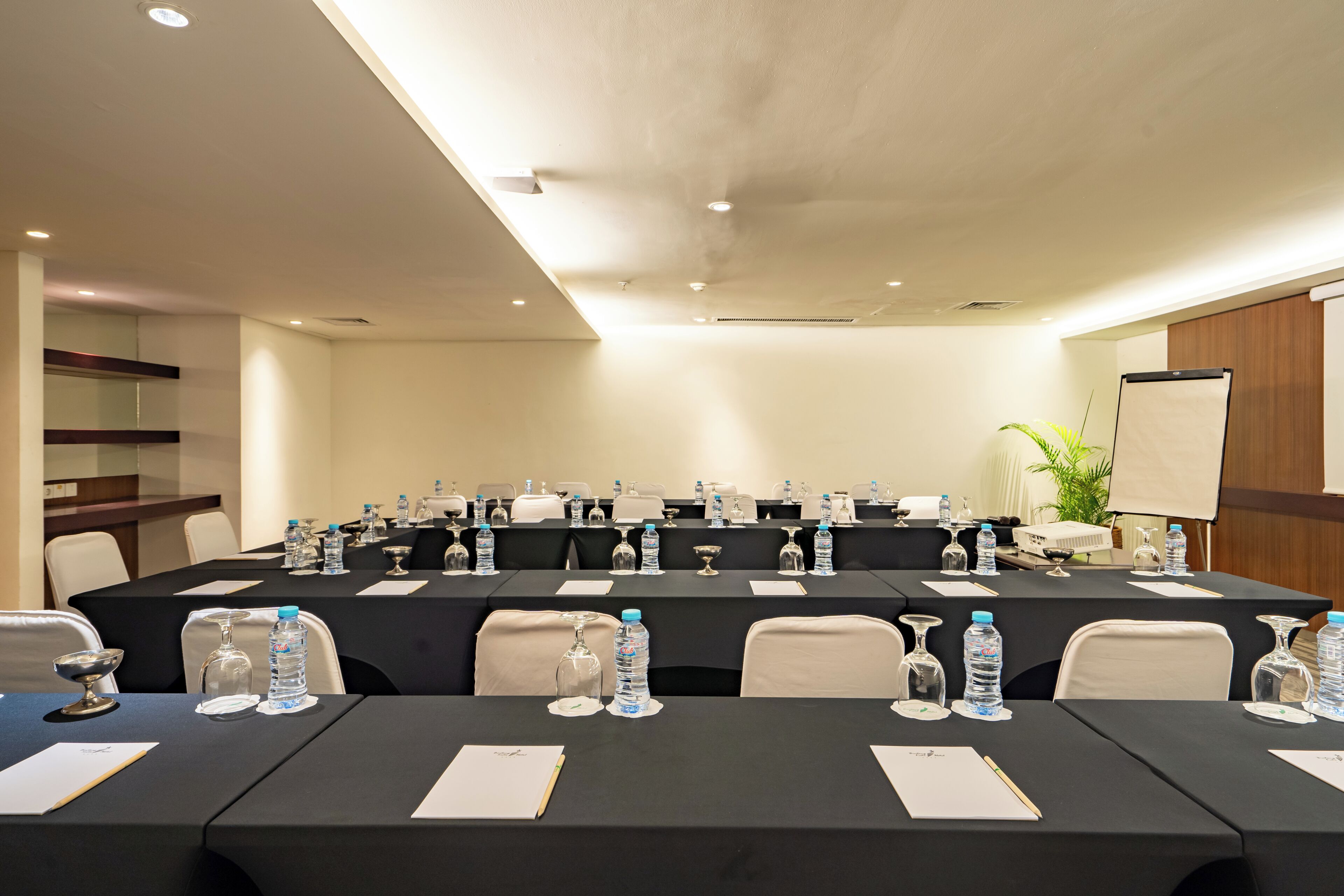 A conference room with a long table, chairs, water bottles, and a projector screen.