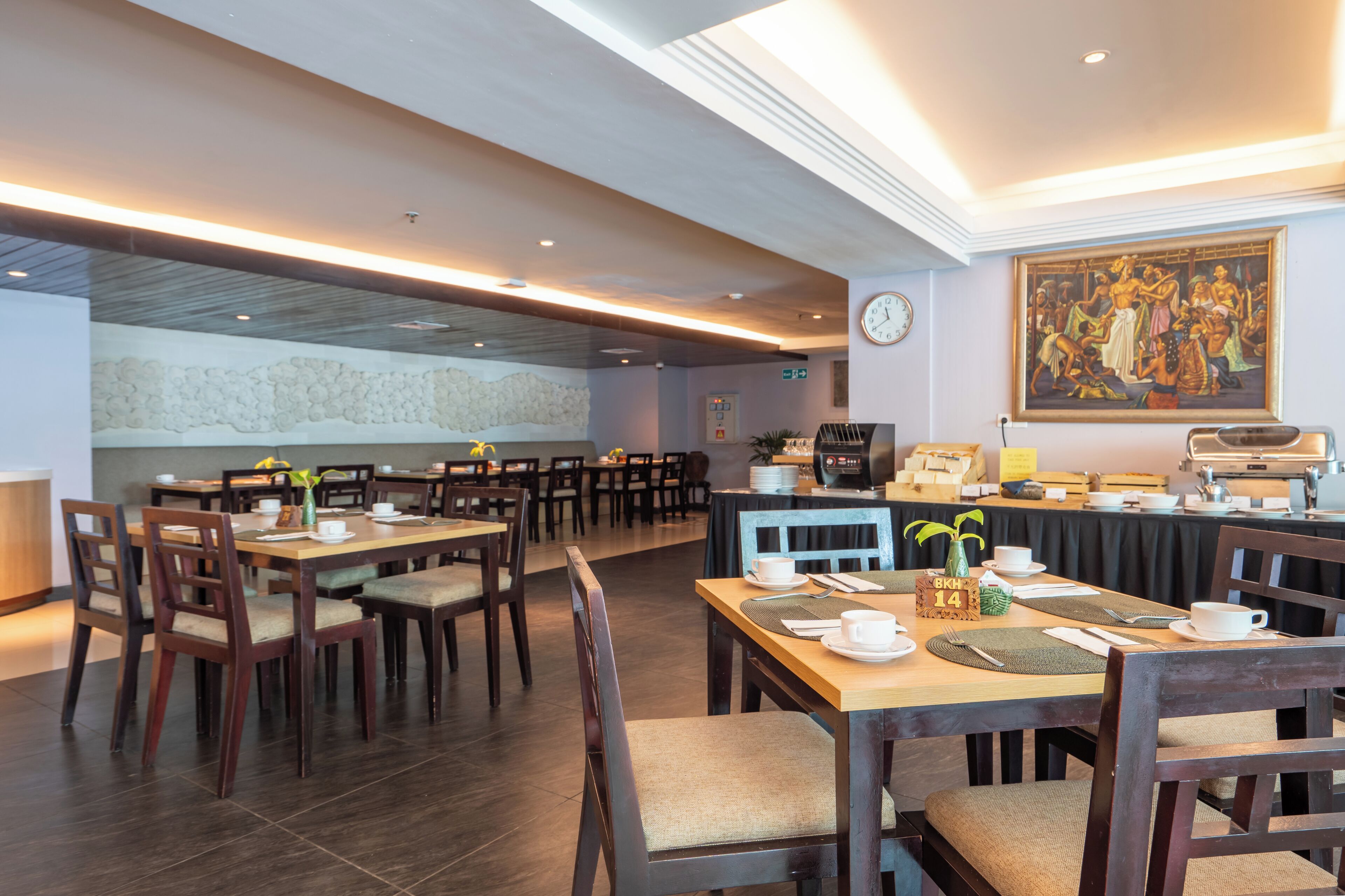 Un restaurante con mesas y sillas de madera, un reloj en la pared y un cuadro sobre el mostrador.