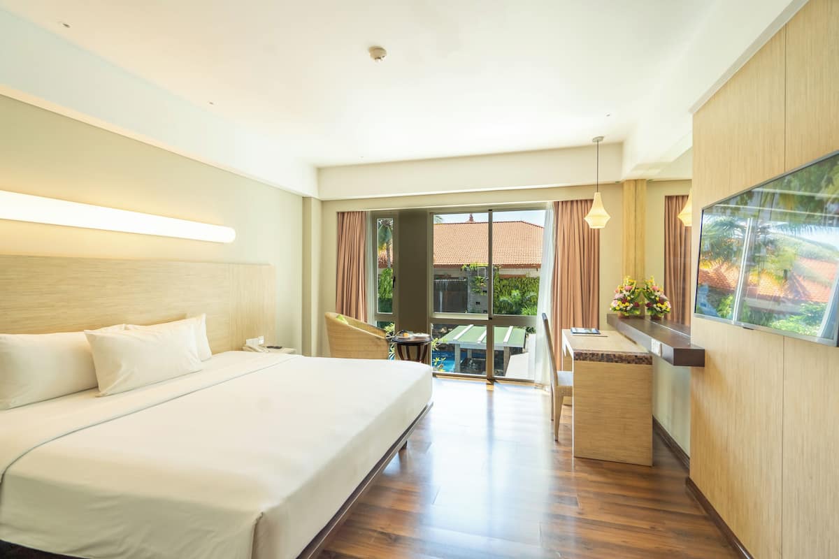 A hotel room with a large bed, a desk, and a view of the outdoor area.