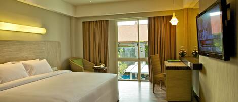 Habitación de hotel con una cama grande, un escritorio, una silla, un televisor y vistas al exterior.