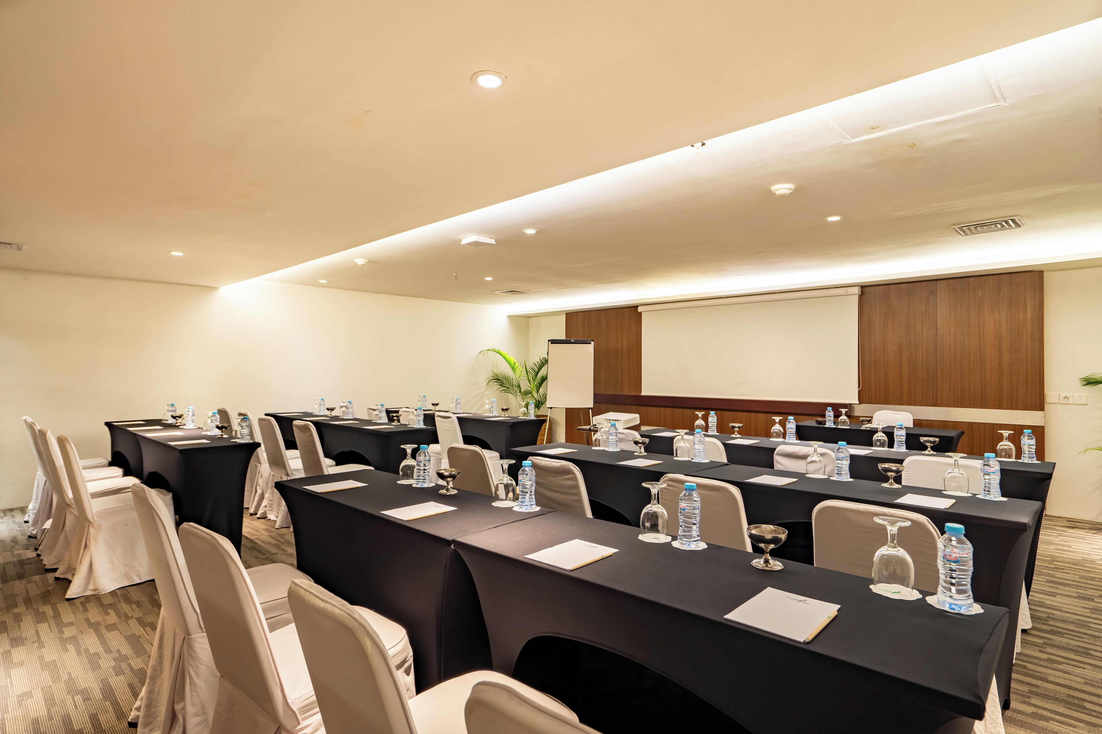 A conference room with multiple tables, chairs, water bottles, and a projector screen.