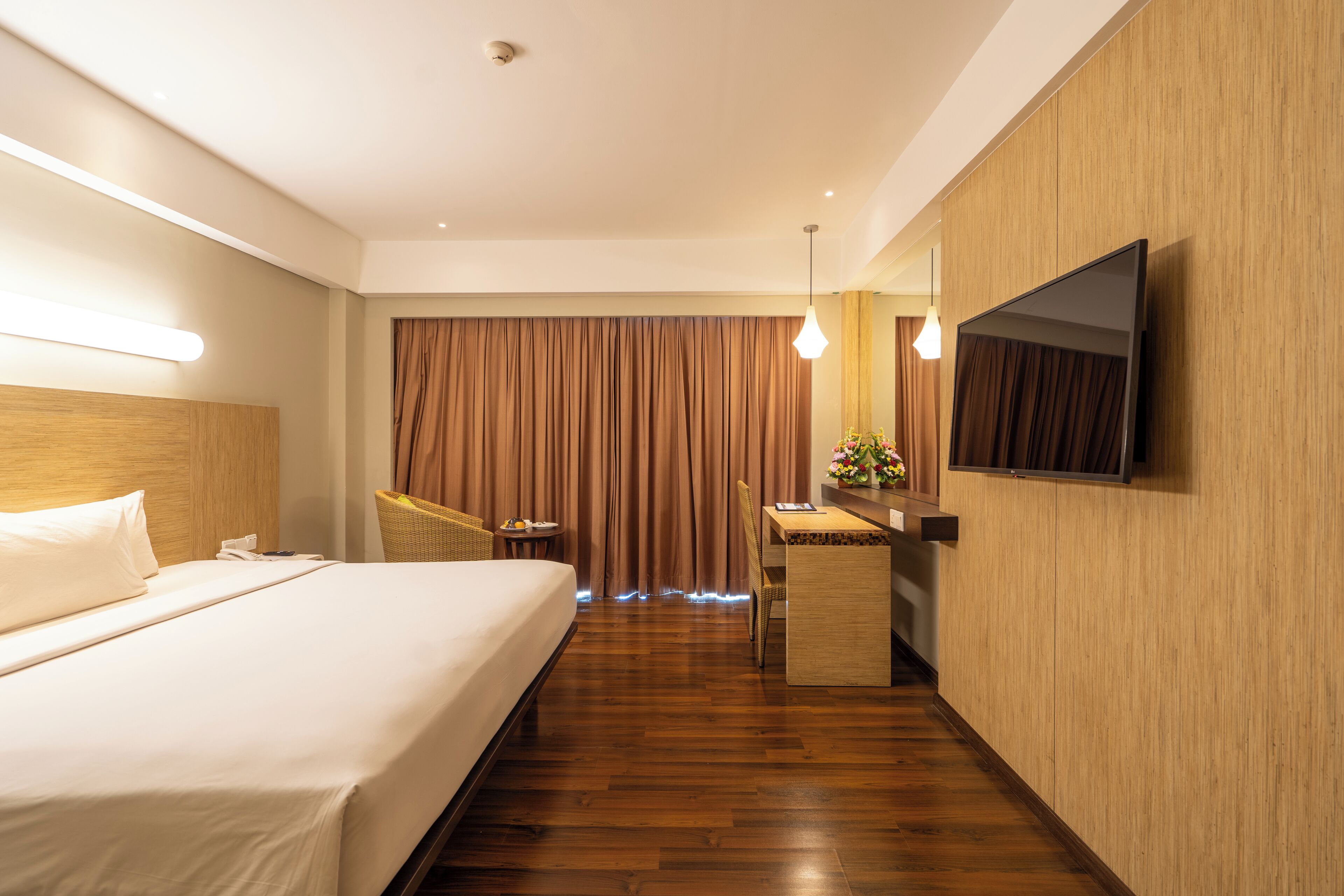Een hotelkamer met een bed, een bureau, een stoel, een televisie en een groot raam met gordijnen.