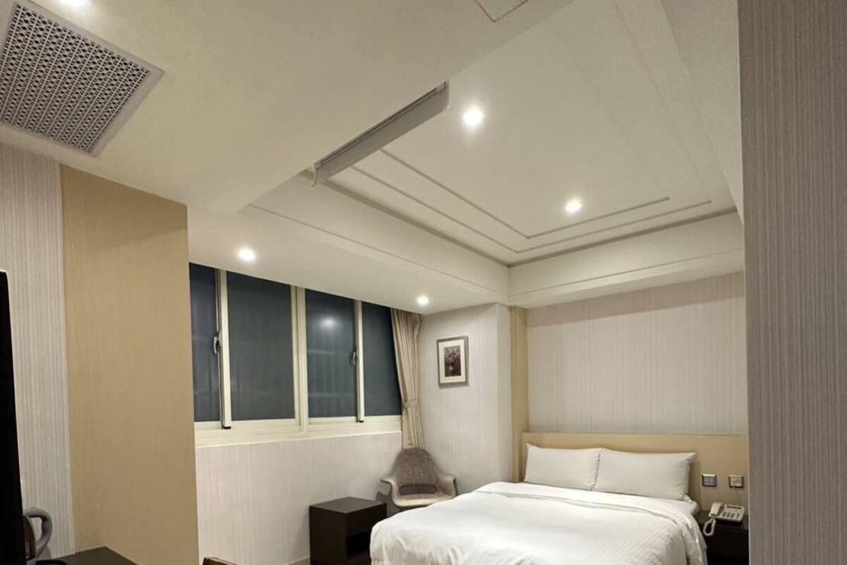 A hotel room with a bed, bedside table, chair, and a desk with a chair.