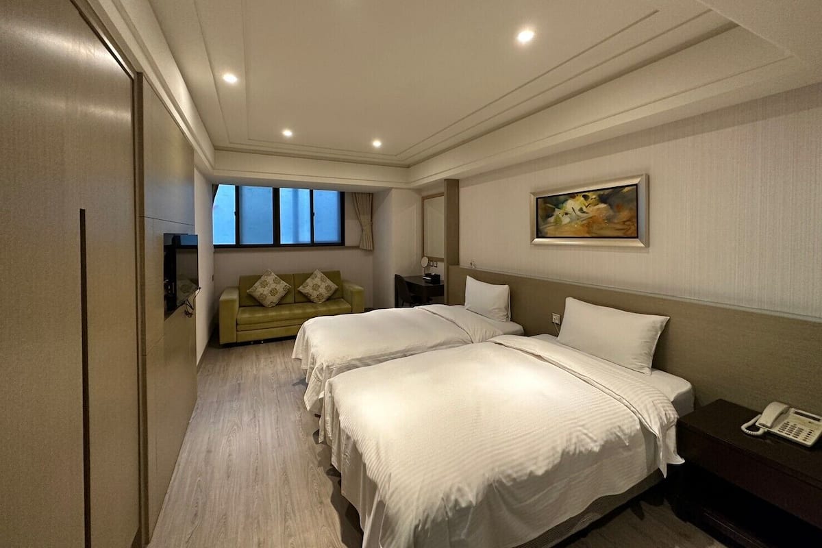 A hotel room with two beds, a sofa, a painting, and a telephone on a nightstand.