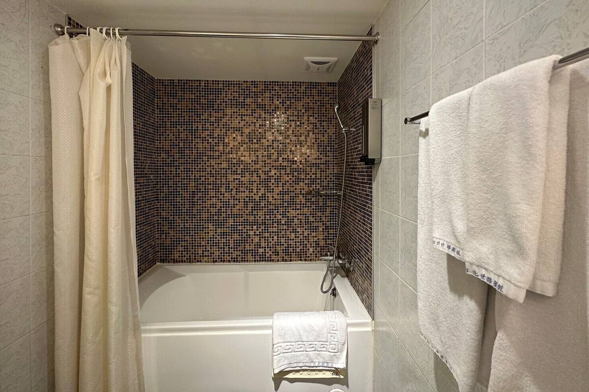 A bathroom with a bathtub, a shower, and a tiled wall.