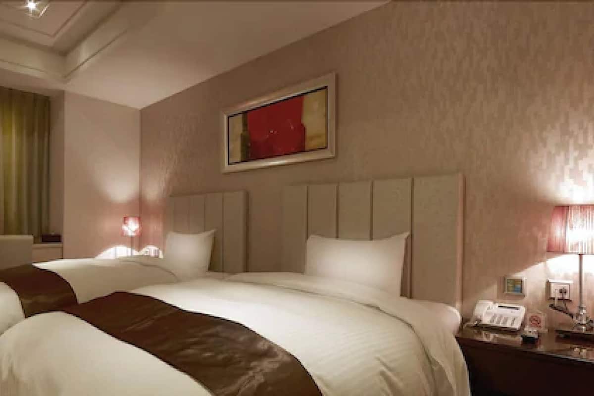 A hotel room with a large bed, two bedside tables, a desk with a telephone, and a window with curtains.