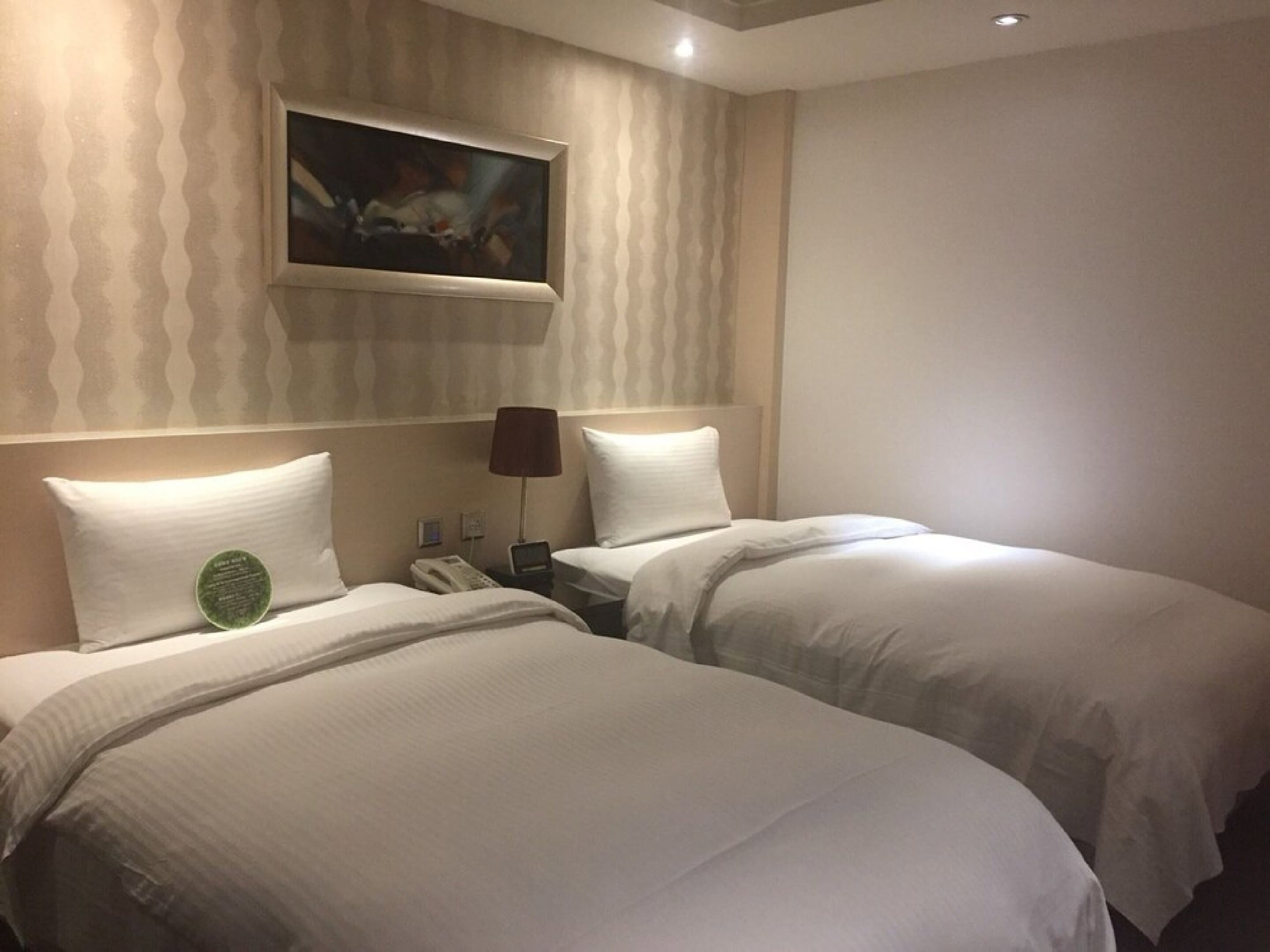 Une chambre d’hôtel avec deux lits, un tableau au mur et une lampe sur la table de chevet.