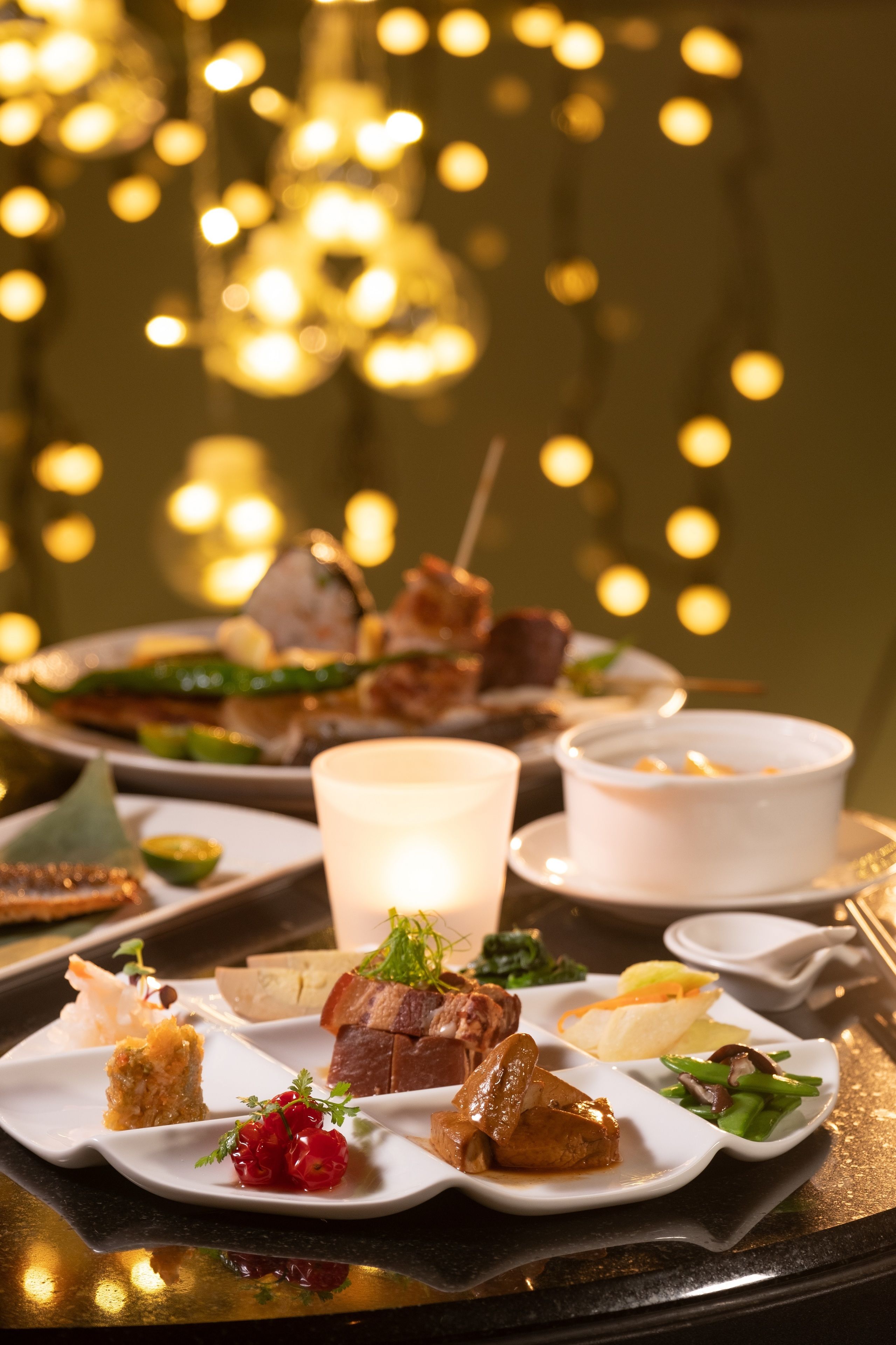 A table set with various dishes, including meat, vegetables, and desserts, with a candle in the center.