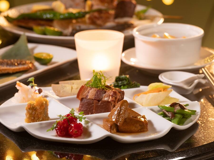 A table set with various dishes, including meat, vegetables, and desserts, with a candle in the center.