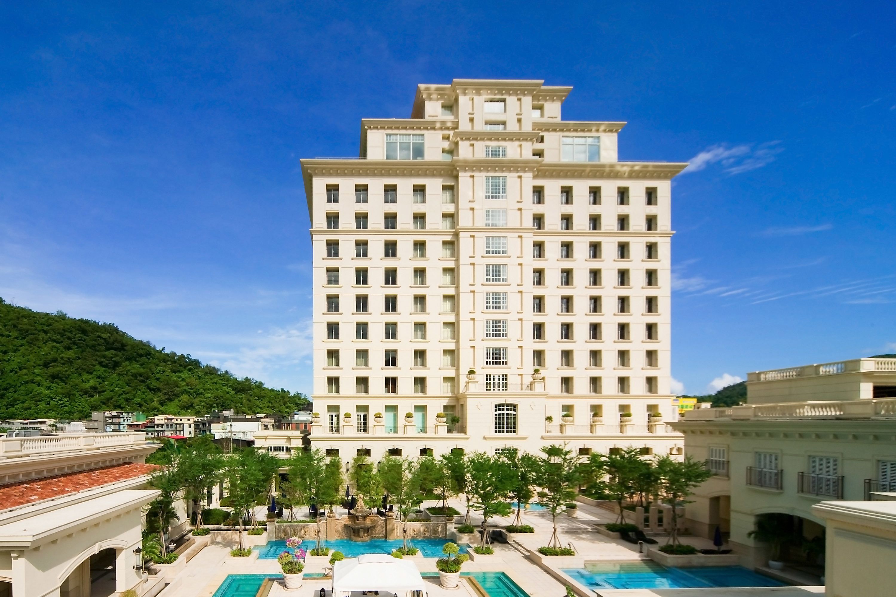 Un grand hôtel à étages, doté d’une cour intérieure avec une piscine et entouré d’une végétation luxuriante.