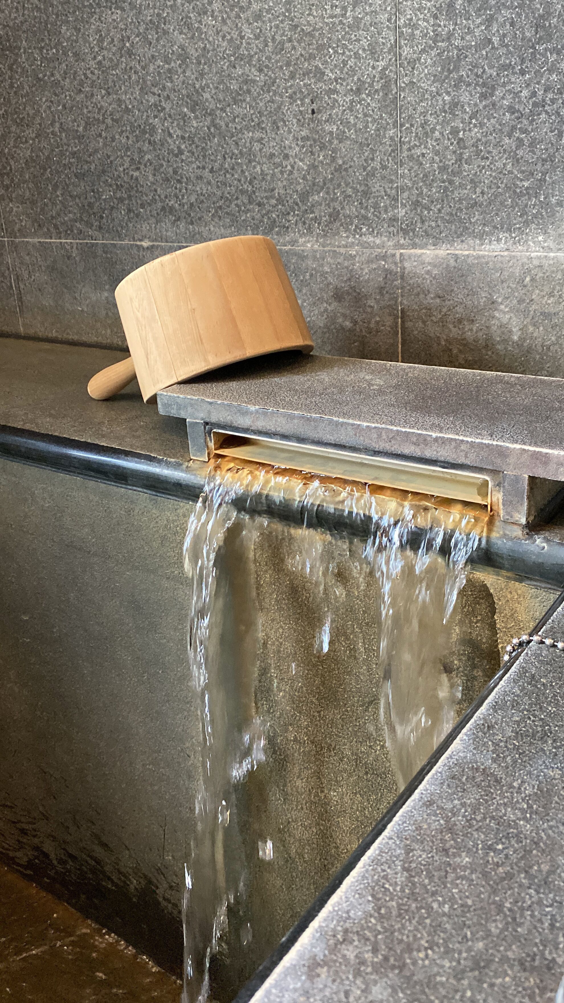 A wooden paddle leaning against a tiled wall with water flowing from a pipe.