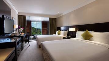 A hotel room with two beds, a desk with a TV, and a view of the outdoors.