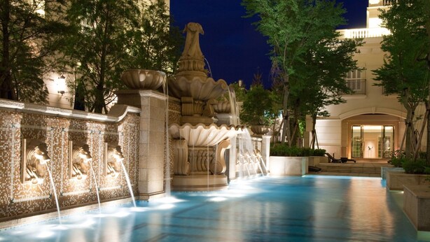 A nighttime pool area with a central fountain, surrounded by trees and a building with a balcony. - RSL Cold & Hot Springs Resort Suao (Suao)