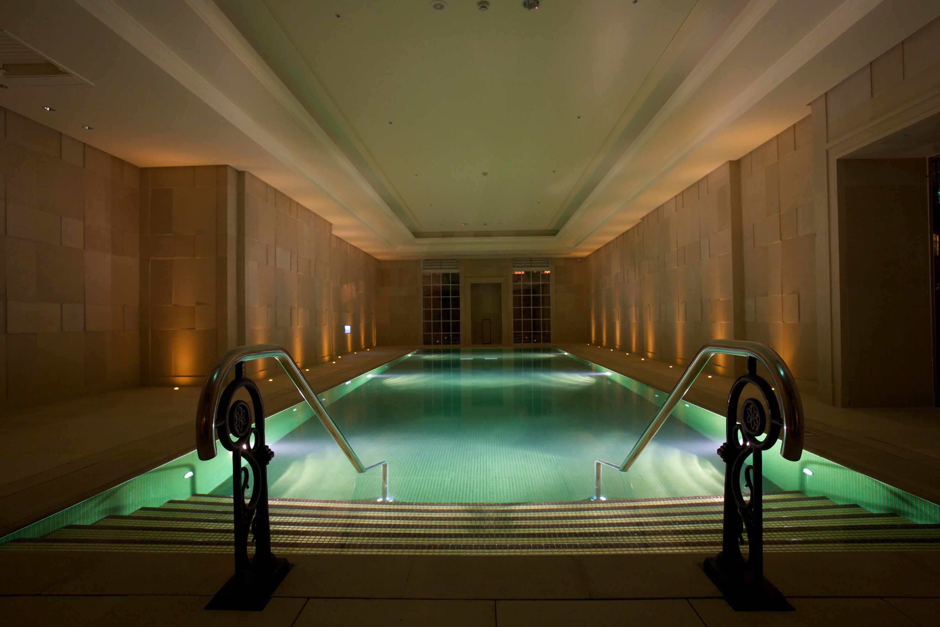 Una amplia piscina interior con una escalera central y una barandilla de vidrio.