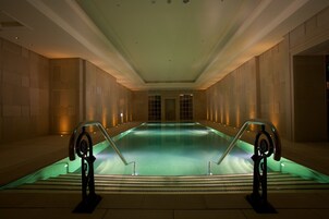 Una amplia piscina interior con una escalera central y una barandilla de vidrio.