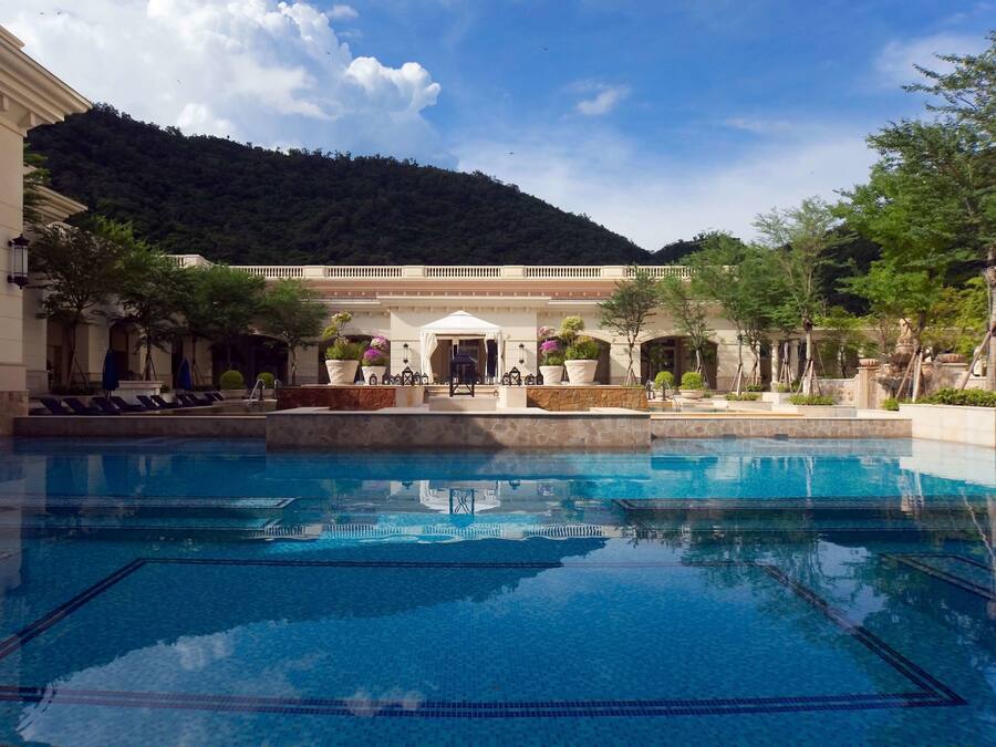 En swimmingpool med klart, blåt vand, omgivet af en bygning med hvid facade og søjler.