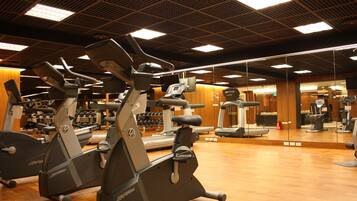 A gym with multiple exercise machines, wooden flooring, and a mirrored wall.
