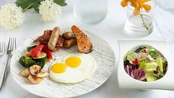 A breakfast plate with eggs, bacon, sausage, and vegetables, a glass of water, and a bowl of salad.