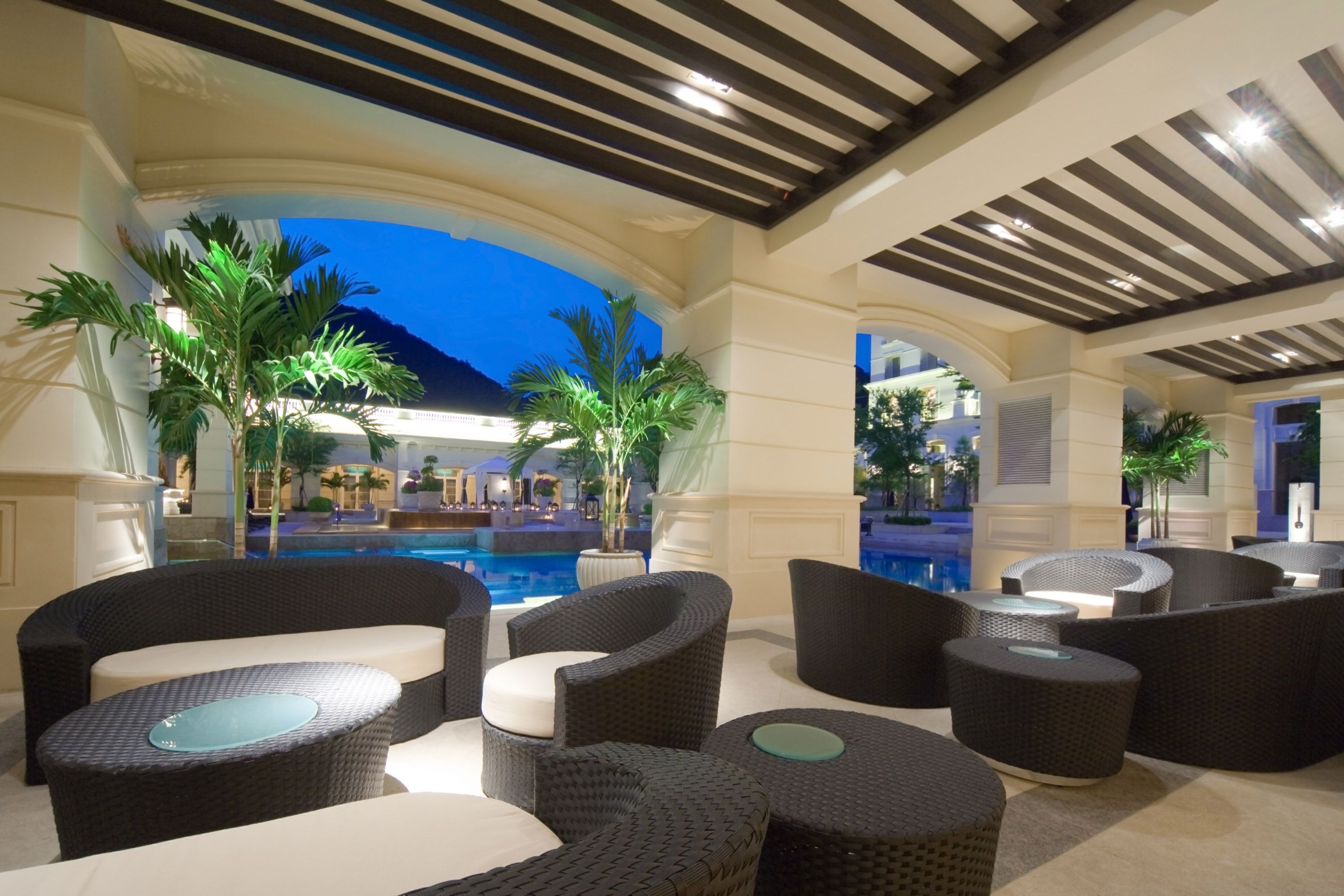 A poolside area with wicker furniture and a view of a pool and mountains.