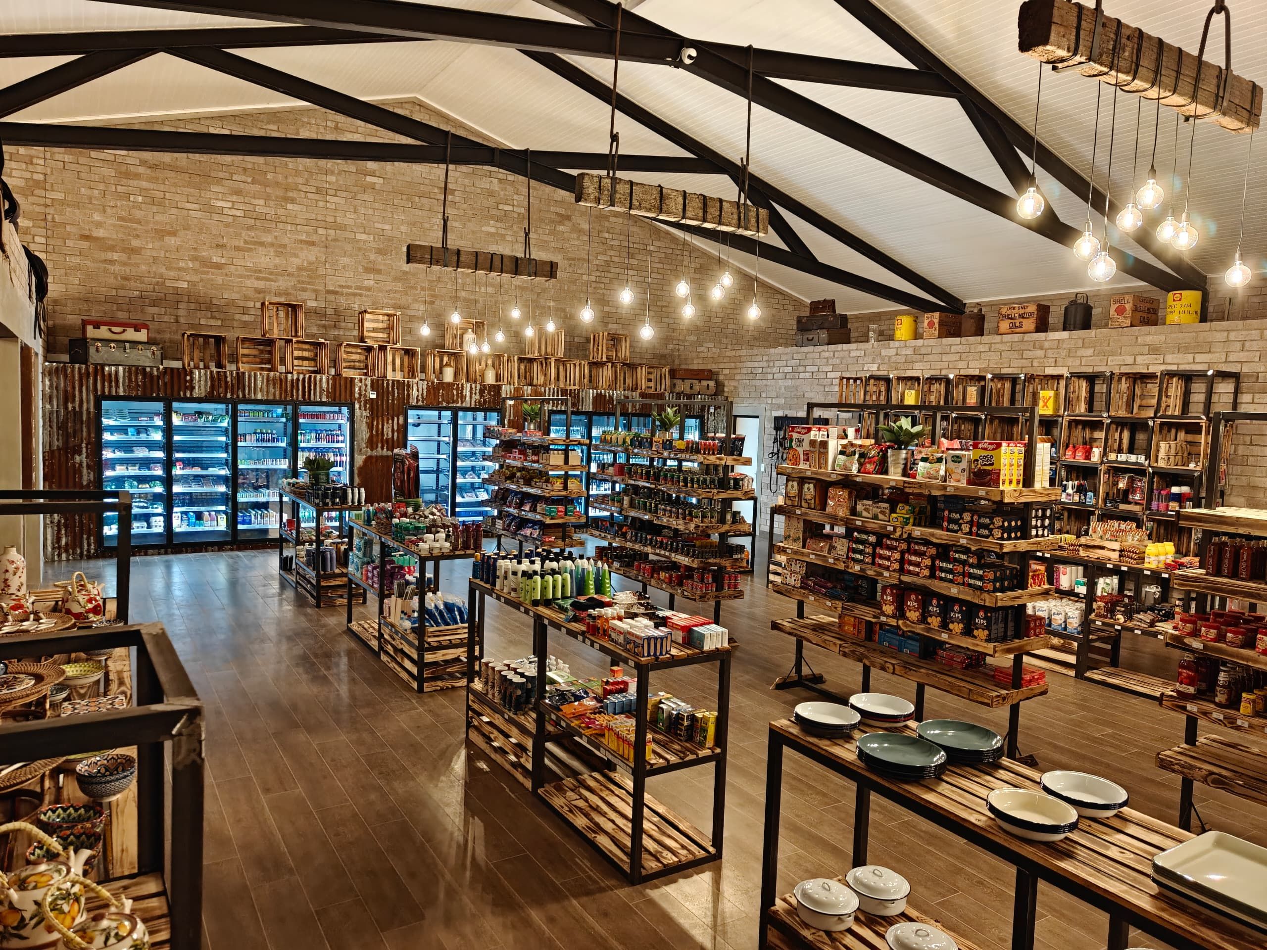 A spacious store with high ceilings, exposed brick walls, and wooden beams. Shelves are stocked with a variety of products, and there are hanging light fixtures.