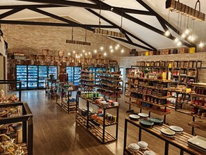 A spacious store with high ceilings, exposed brick walls, and wooden beams. Shelves are stocked with a variety of products, and there are hanging light fixtures. - Sossus Oasis Camp Site (Sesriem)