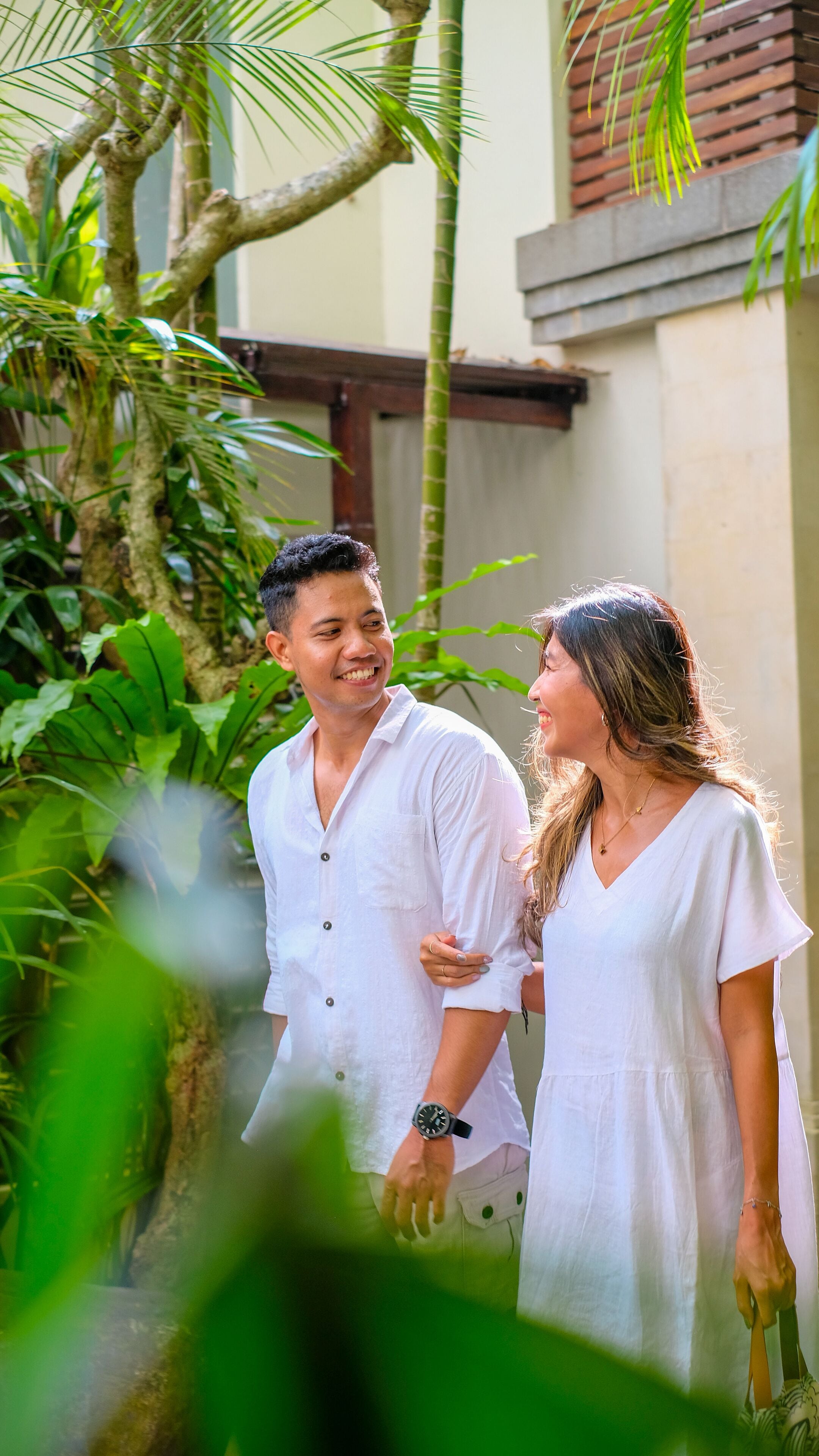 A couple standing in a lush garden with a building in the background.