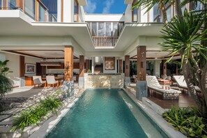 A modern pool area with a clear view of the pool, lounge chairs, and a dining area with tables and chairs.