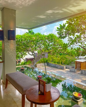A serene indoor garden with a water feature, a bench, and a table with a framed picture and a bowl of flowers.
