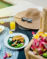 A dining table with a straw hat, sunglasses, a glass of orange juice, and plates of food.
