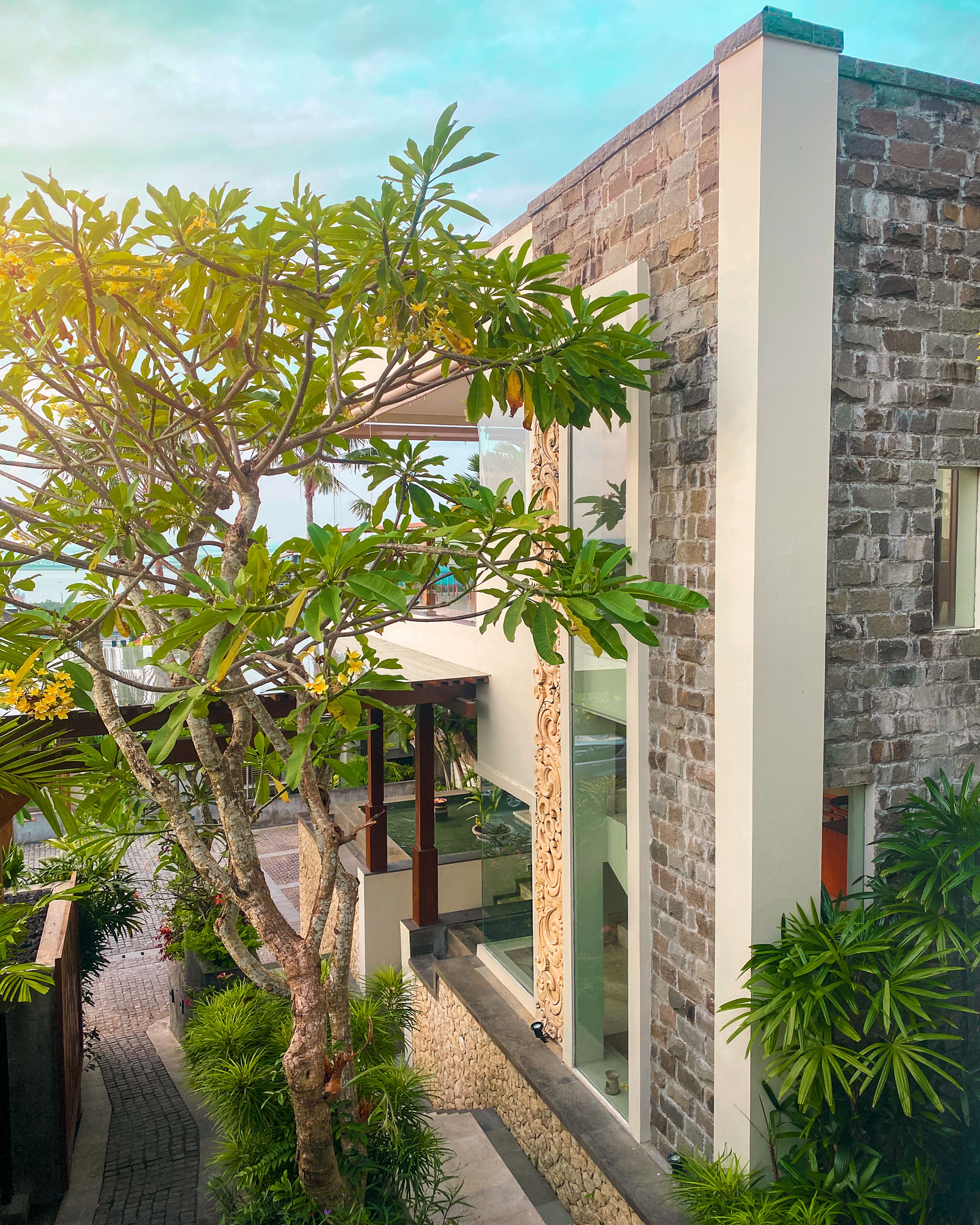 Un edificio moderno con fachada de piedra, ventanas amplias y un árbol en primer plano.
