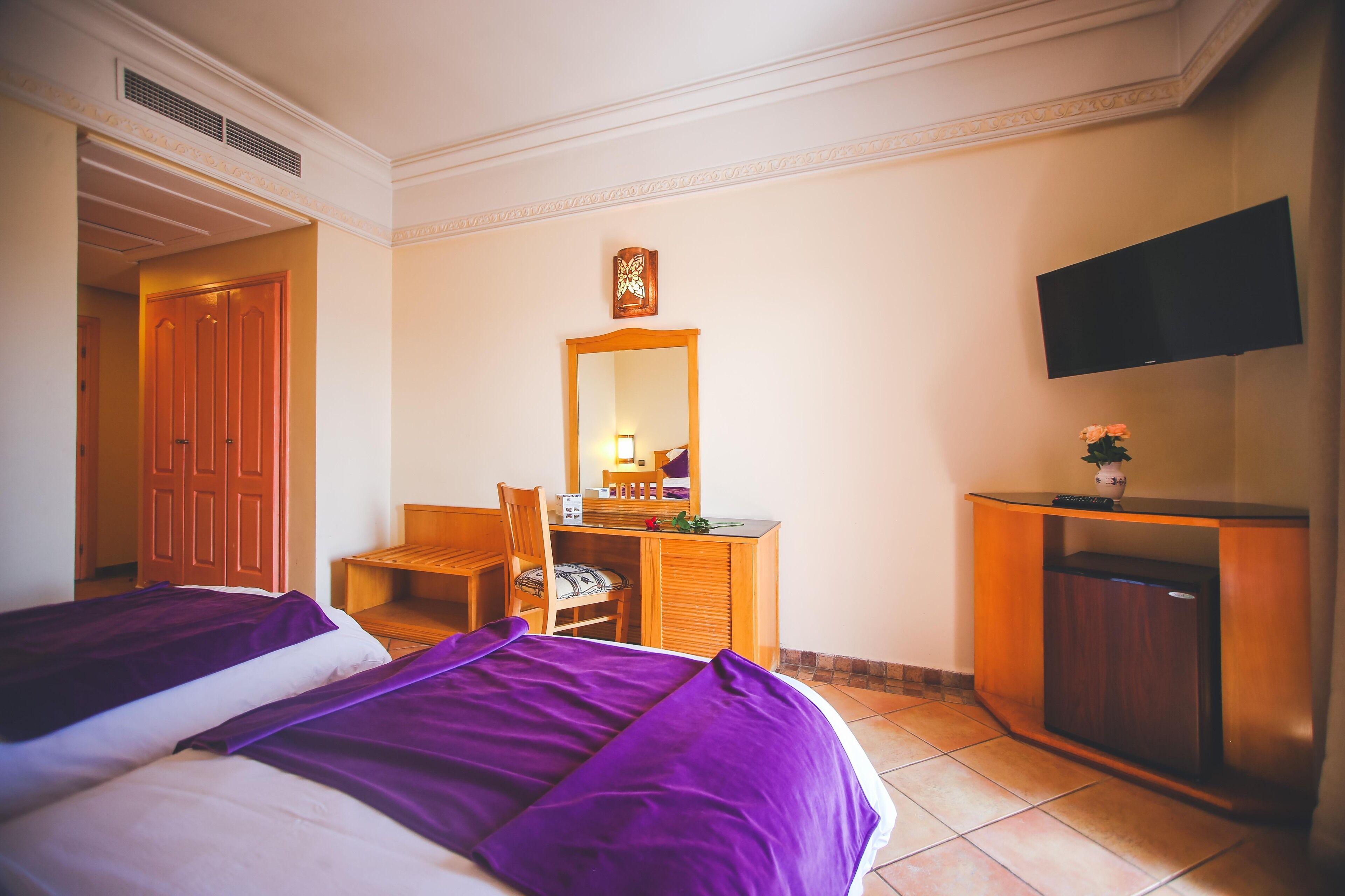 Une chambre d’hôtel avec deux lits, un bureau, une chaise, une commode, une télévision et une porte.
