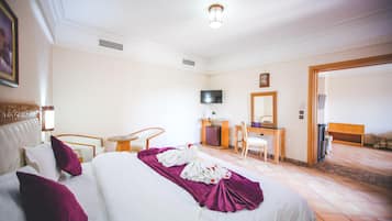 Una camera d'albergo con un letto, una scrivania, una sedia, una televisione e una porta che dà su un'altra stanza.