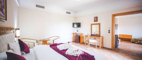 Quarto de hotel com cama, escrivaninha, cadeira, televisão e porta que dá para outro aposento.