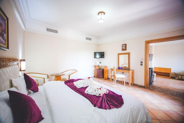 Habitación de hotel con cama, escritorio, silla, televisor y puerta que da a otra habitación.