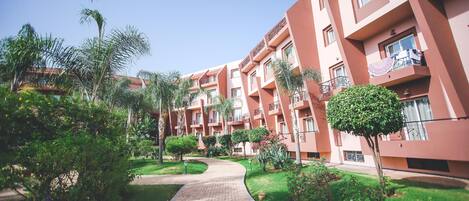 Un sendero conduce a un edificio con varios balcones y un jardín bien cuidado con diversas plantas y árboles.