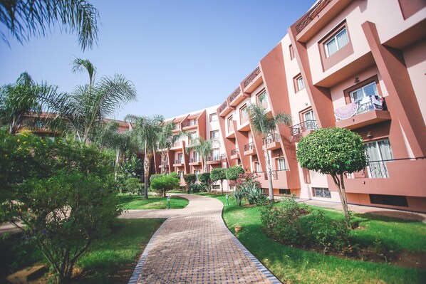 Un sendero conduce a un edificio con varios balcones y un jardín bien cuidado con diversas plantas y árboles.