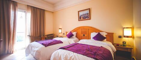 Habitación de hotel con dos camas, una silla, una mesa y un cuadro en la pared.